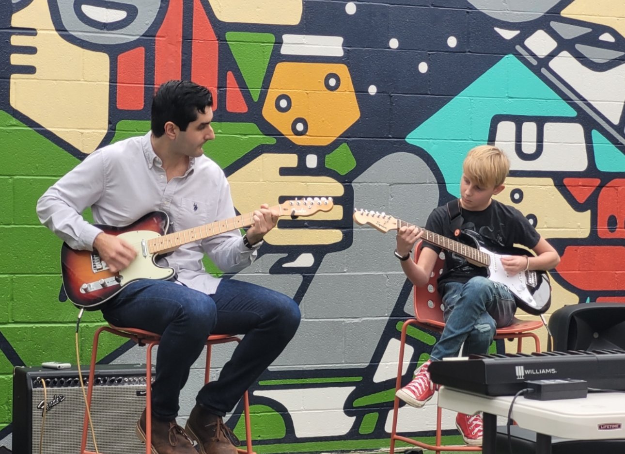 Adam playing guitar alongside a young student